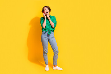 Full length photo of excited impressed lady wear green shirt communicating modern gadget looking empty space isolated yellow color background