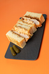 Large appetizing sandwich with chicken and pickled cucumbers on an orange background.