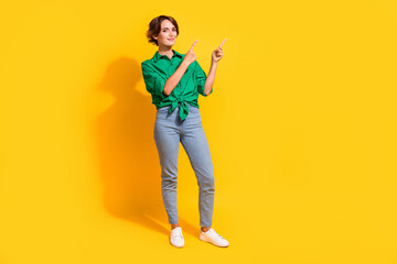 Fototapeta na wymiar Full length photo of pretty positive lady wear green shirt showing two fingers empty space isolated yellow color background