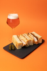 Large appetizing sandwich with chicken and pickled cucumbers on an orange background.