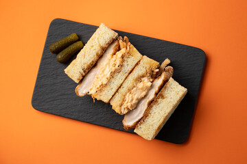 Large appetizing sandwich with chicken and pickled cucumbers on an orange background.
