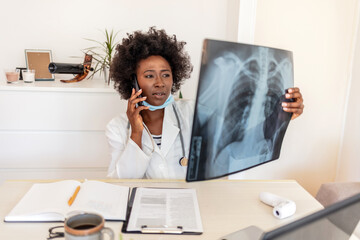 Young doctor with smartphone looking at chest x-ray in her office. Female doctor examining an...