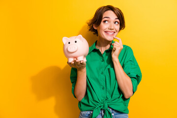 Photo of positive dreamy lady wear green shirt finger chin rising pig money box looking empty space...