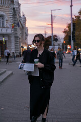 Stylish girl with newspaper walking in city at the evening.