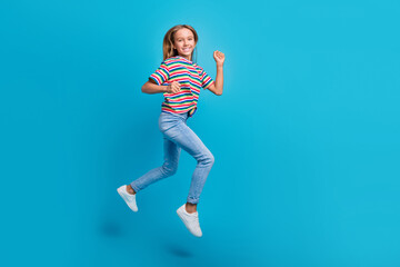 Full length photo of satisfied cute small schoolgirl dressed striped t-shirt run at sale empty space isolated on blue color background