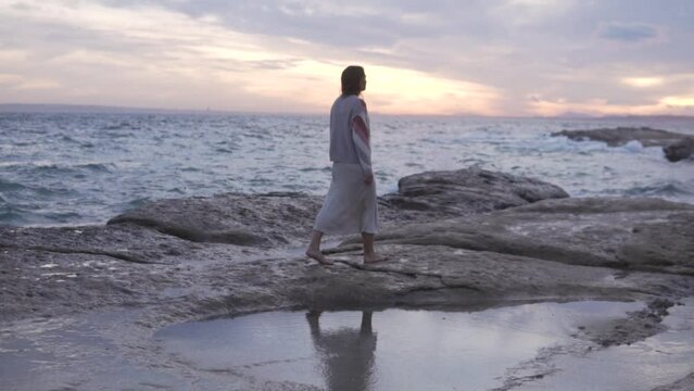 Woman in sweater walking on the beach at sunset.