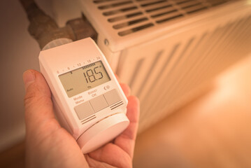 Zum Energiesparen wird elektronisches Thermostat an Heizung auf 18,5 Grad Raumtemperatur eingestellt