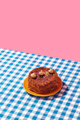 Chocolate delicious cake on plate on blue checkered tablecloth over pink background. Concept of...