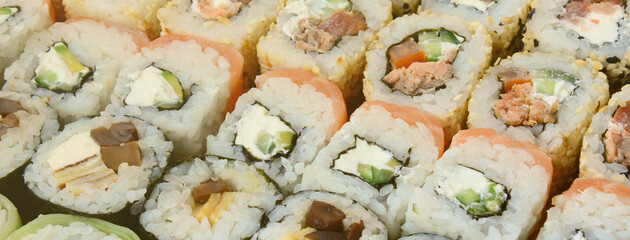 Close-up of a lot of sushi rolls with different fillings lie on a wooden surface. Macro shot of...