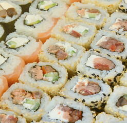 Close-up of a lot of sushi rolls with different fillings lie on a wooden surface. Macro shot of...