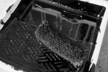 Paint roller in tray with black industrial paint or primer. Top view of paint roller with paint...
