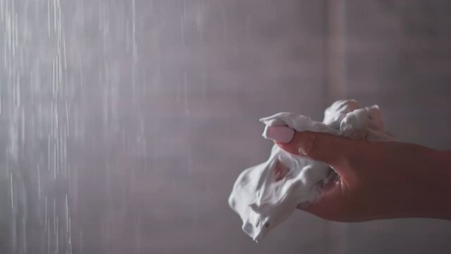 Woman squishes body mousse by palm in bathroom closeup. Lady hand whips skin care soft foam in shower cabin. Organic cosmetic product for spa