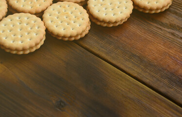 A round sandwich cookie with coconut filling lies in large quantities on a brown wooden surface. Photo of edible treats on a wooden background with copy space