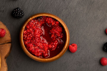 crumpled juicy red raspberries in a wooden bowl