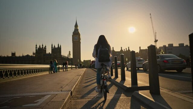 Young tourist woman riding bicycle on Westminster Bridge London towards Big Ben at sunset. Urban cycle chic and ecological transportation by bike in London