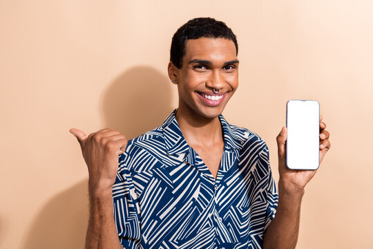 Photo portrait of nice young male hold device point empty space dressed stylish blue print garment isolated on beige color background