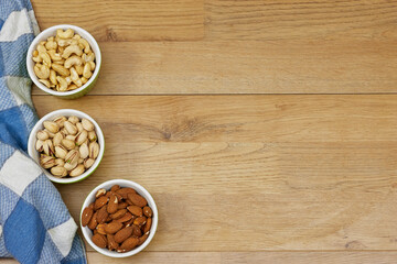 Obraz na płótnie Canvas nuts (almonds, pistachio, cashews) in bowls on wooden table