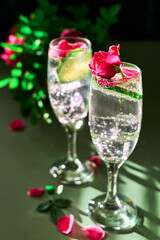 Delicious refreshing champagne drink with lemon and roses on green background. Sparkling wine with flowers and lime of rose lemon spritzer for romantic events.