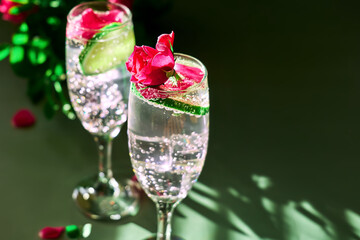 Delicious refreshing champagne drink with lemon and roses on green background. Sparkling wine with flowers and lime of rose lemon spritzer for romantic events.