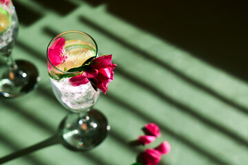 Delicious refreshing champagne drink with lemon and roses on green background. Sparkling wine with...