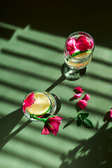 Delicious refreshing champagne drink with lemon and roses on green background. Sparkling wine with flowers and lime of rose lemon spritzer for romantic events.