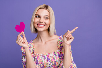 Photo of shiny dreamy lady wear flower print top rising pink heart pointing empty space isolated violet color background