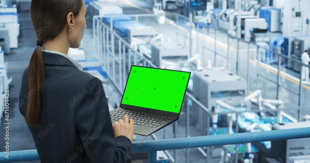 Aufkleber Female Technician Using Laptop Computer with Green Screen Chroma Key Mock Up Display and Looking Around a Factory Facility with Robotic Arms Producing Modern Electronic Components for Tech Industries