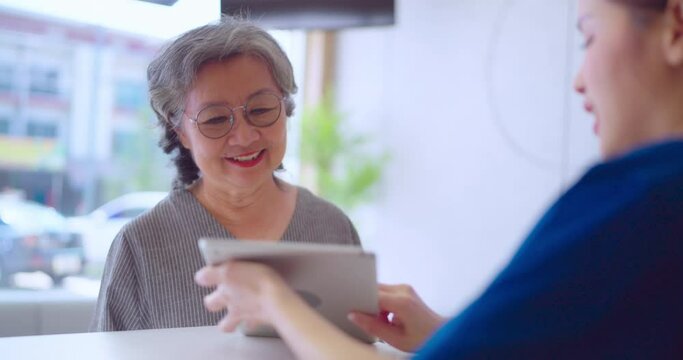 Beautiful asian nurse talking with senior woman patient with smile in hospital. She making appointment with senior woman at counter.