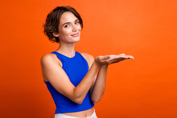 Photo of cute cheerful lady wear blue singlet showing arms empty space isolated orange color background