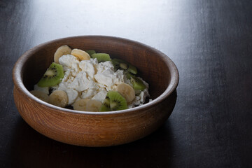 Homemade diet cheese on a wooden plate with banana and kiwi. Delicious homemade food
