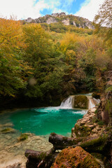 Fototapeta na wymiar The waterfalls and crystal clear, blue, turquoise and green waters of the Nacedero del Urederra, with its beech forest with its autumn colors in the Sierra de Urbasa-Andía. Navarre. Spain
