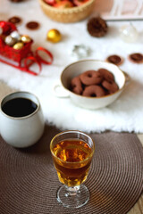 Cup of tea or coffee, glass of wine or juice, bowl of cookies, organic pomegranate, fluffy blanket, pine cones, various Christmas decorations and lit candles on the table. Christmas hygge concept.