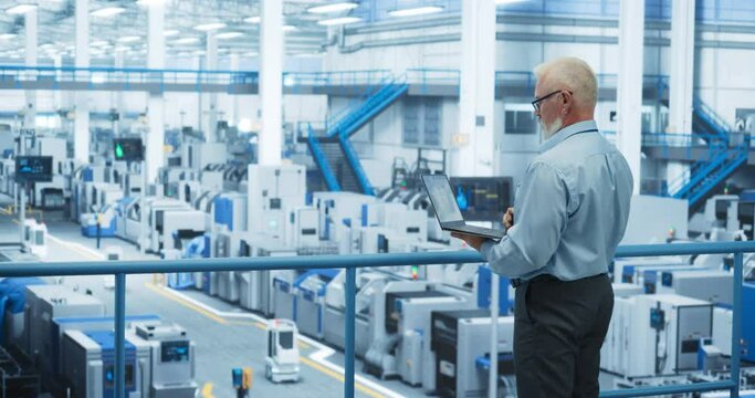 Electronics Manufacturing Technician Working on a Laptop Computer at a Factory Space. Specialist Developing, Maintaining, Fine-Tuning Programs for Machine Production and Assembly