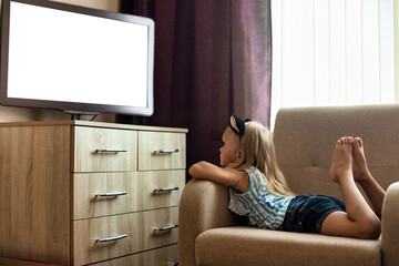 Funny little girl child 5-6 year old lying down on chair and watching tv, empty isolated screen....