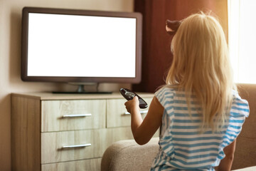 Rear view of little girl kid 5-6 year old with remote control watching tv in room look movie....