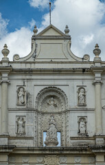 Fototapeta na wymiar Guatemala, La Antigua - July 20, 2023: Closeup of free standing white front facade top with 6 statues of Mary, God himself, apostles, and saints under blue cloudscape