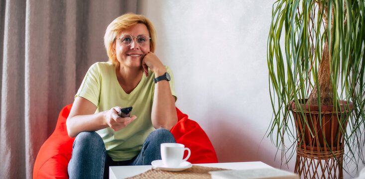 Close Up Photo Of Mature Beautiful Woman Using Remote Control While Watching Tv Sitting On Sofa At Home And Resting