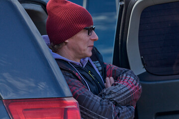 A mature man sits in the trunk of a car and rests. Take a break from kitesurfing. Cold windy autumn day.