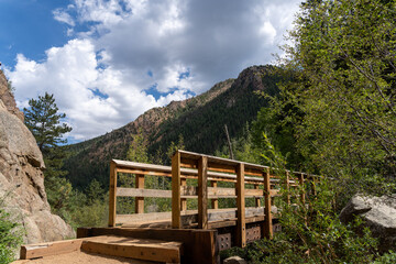 A bridge on the Seven Bridges Trail in North Cheyenne Cañon Park in Colorado Springs, CO in the late afternoon on a sunny summer day, with trees, red rocks, and mountains in the landscape