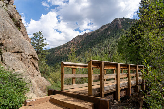 A bridge on the Seven Bridges Trail in North Cheyenne Ca&ntilde;on Park in Colorado Springs, CO in the late afternoon on a sunny summer day, with trees, red rocks, and mountains in the landscape