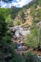 A waterfall cascade on the Seven Bridges Trail in North Cheyenne Cañon Park in Colorado Springs, CO in the late afternoon on a sunny summer day, with trees, red rocks, and mountains in the landscape