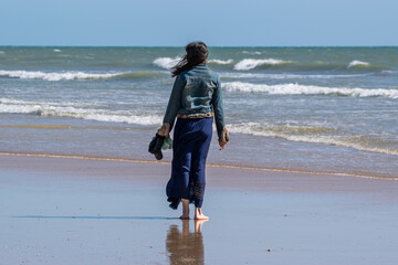 A young woman with long brown hair, dressed in a blue jeans jacket and long blue skirt, contemplates the ocean from Oiseaux beach, Saint Jean de Monts, Vendée, FRANCE.