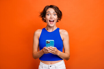 Photo of pretty excited lady wear blue singlet getting message modern device isolated orange color...