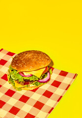 Delicious homemade burger, hamburger with fresh bun, meat, cheese, lettuce and tomato on checkered napkin on yellow background. Concept of fast food, taste, junk food. Complementary colors. Poster, ad
