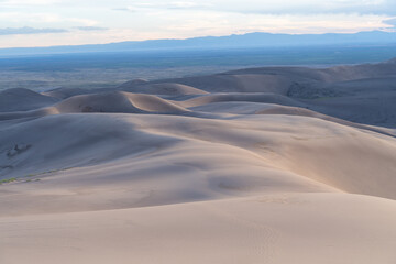 View from the top at golden hour and sunset at Great Sand Dunes National Park in Colorado on a sunny summer evening, with mountains in the background