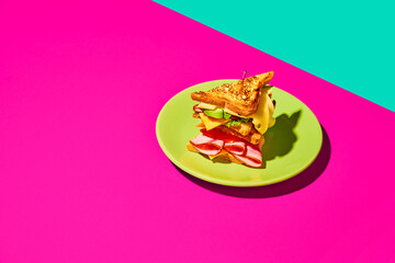 Club sandwich with grilled bread, ham, lettuce, cheese, tomato and avocado over pink green background. Breakfast. Concept of fast food, taste, cooking, ingredients. Complementary colors. Poster, ad