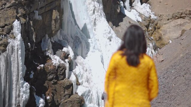 Defocused tourist woman looking at frozen waterfall during winter in Spiti Valley, Himachal Pradesh, India. Winter scene in north India.