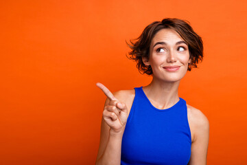 Photo of young cheerful attractive lady indicate finger empty space showing benefits travelers life isolated on orange color background