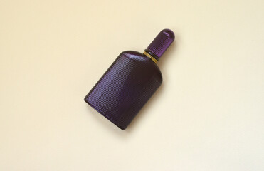 Dark purple perfume bottle with golden ribbon on pastel paper background. Trendy fragrance.