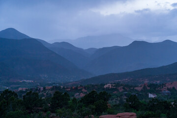 Fototapeta premium A view of a rainstorm over Pike's Peak and other blue misty mountains on a cloudy summer evening, as viewed from Garden of the Gods in Colorado Springs, CO